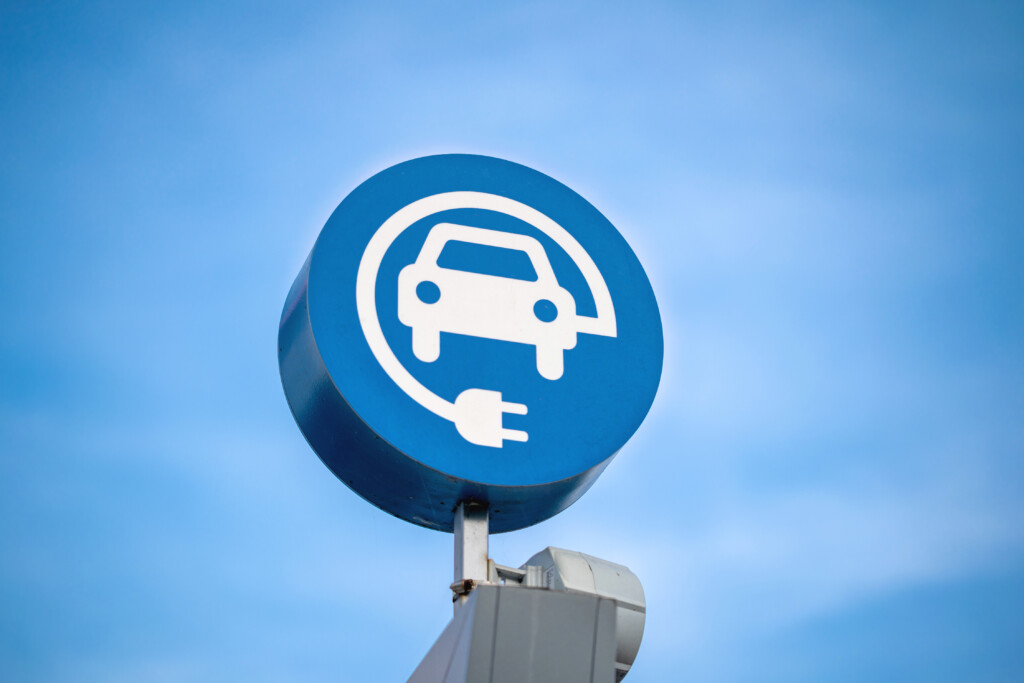 electric vehicle charging sign, blue sky background, EV, Image by Adobe Stock
