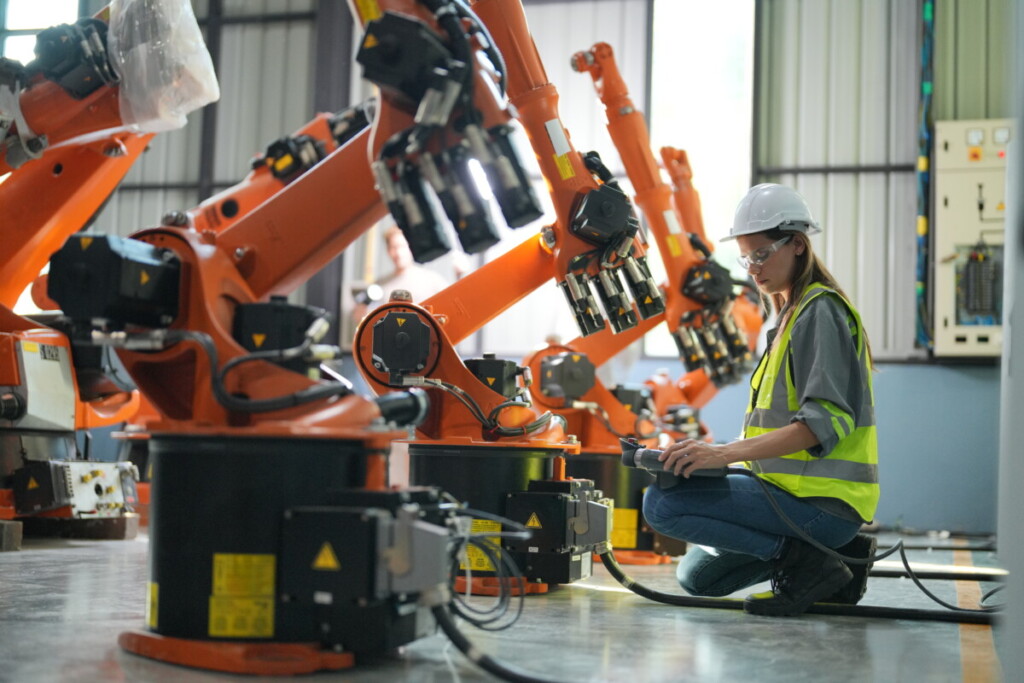 Robotic Arm engineer check on equipment in its with software of an Artificial Intelligence, Programming development technology work. Female industrial engineer working at automated AI robotic production factory.